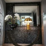 Elegant entrance foyer of Dr. Songabau's practice with a black marble wall, a mirror reflecting the clinic's signage, white orchids in a black bowl, and a modern gold lamp on a console table - Louis Pasteur Private Hospital, Pretoria, South Africa.