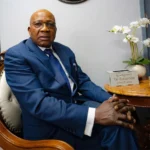 Professional portrait of Dr. Songabau, Obstetrician and Gynecologist (OB/GYN) in Pretoria, sitting in an armchair wearing a blue suit and glasses.
